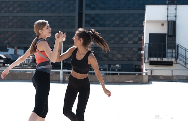 Twee vrolijke vrouwen in fitness dragen high five tijdens het hardlopen in de stad.