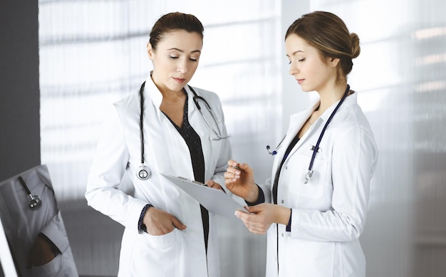 Twee vrouwelijke artsen bespreken de medische tests van hun patiënt terwijl ze in een kliniekkantoor staan. Artsen gebruiken een klembord op het werk. Teamwerk in de geneeskunde.