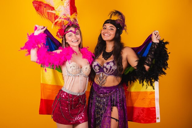 Twee vrouwelijke braziliaanse vrouwelijke vrienden die carnavalsoutfits dragen en de lgb-vlag vasthouden