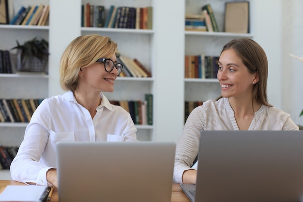 Twee vrouwelijke collega's die met laptop werken en nieuw project bespreken.