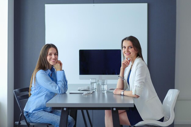 Twee vrouwelijke collega's op kantoor zittend op het bureau