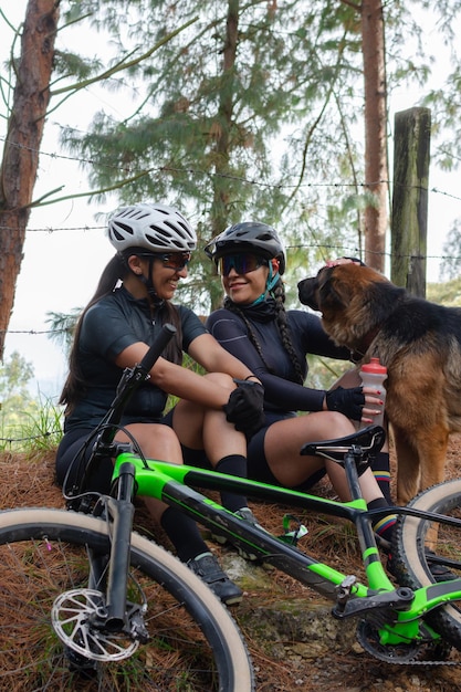 Twee vrouwelijke fietsers zitten te rusten en drinken water terwijl ze een hond aaien