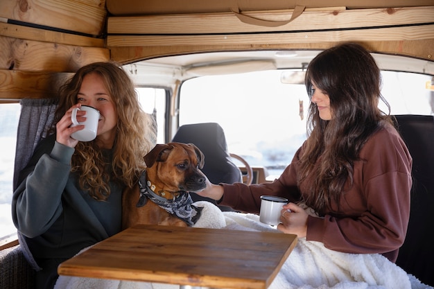 Foto twee vrouwelijke geliefden die koffie drinken en hun boxer aaien tijdens de winterreis in een camper