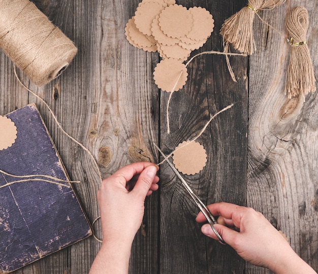 Twee vrouwelijke handen en papieren labels met een bruin touw op grijze houten tafel