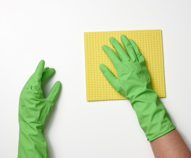 Twee vrouwelijke handen in rubberen beschermende handschoenen voor het schoonmaken houden een gele spond op een witte achtergrond