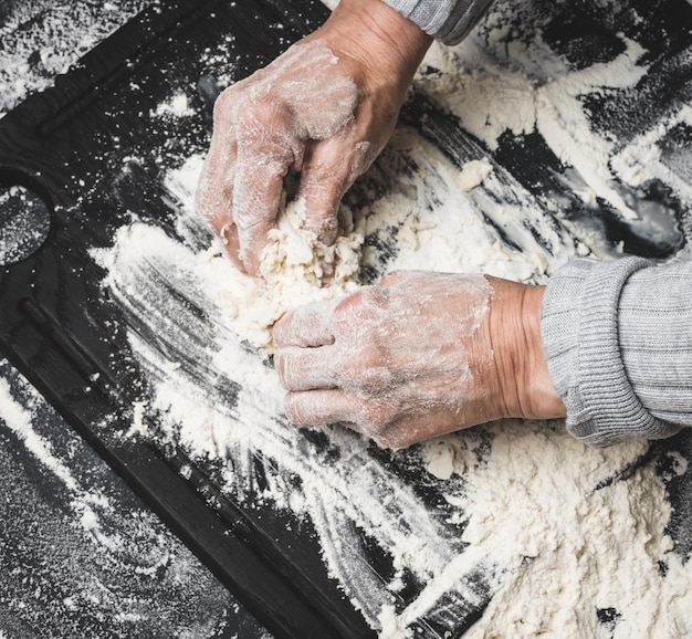 Twee vrouwelijke handen kneden het deeg van witte tarwebloem op een zwart tafelblad