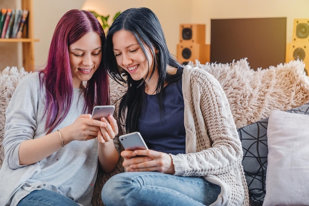 Twee vrouwelijke kamergenoten die hun smartphones thuis online gebruiken en op de bank zitten