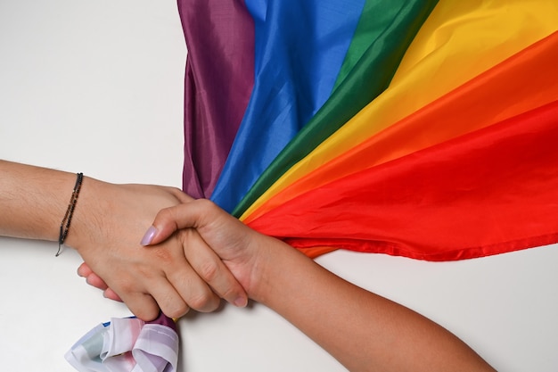 Twee vrouwelijke LGBT-lesbische handen houden elkaar vast boven de LGBT-trotsvlag.