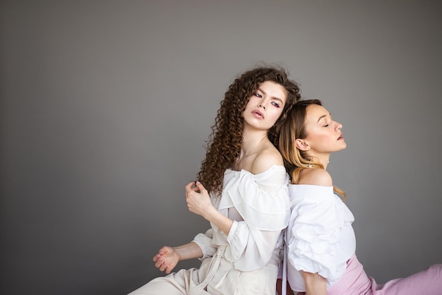 Twee vrouwelijke modemodellen op grijze achtergrond studio portret Twee jonge stijlvolle meisjes poseren