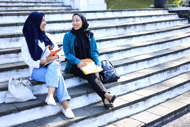 Twee vrouwelijke moslim Indonesische studenten die met elkaar glimlachen en praten