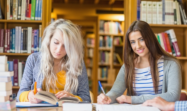 Twee vrouwelijke studenten die nota&#39;s schrijven bij bibliotheekbureau