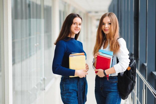 Twee vrouwelijke studenten staan met boeken in de gang van het college