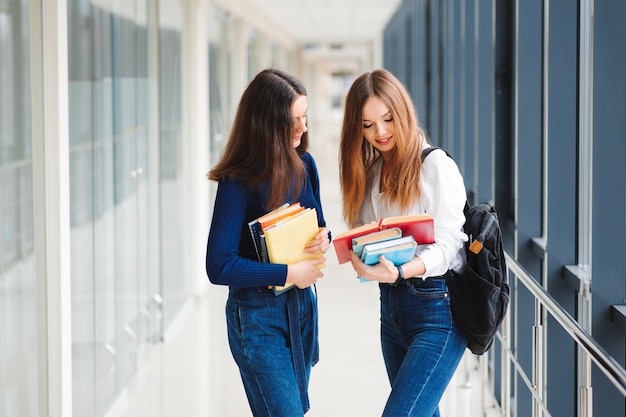 Twee vrouwelijke studenten staan met boeken in de gang van het college