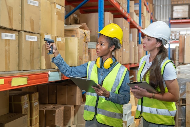 Twee vrouwelijke werknemer werknemer in veiligheidsvest en helm met behulp van tablet en scanner barcode controleren oude producten reserveonderdelen op plank in industrie fabrieksmagazijn