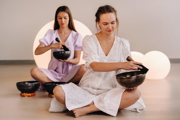 Twee vrouwelijke yogadocenten spelen een Tibetaanse kom in de sportschool tijdens een yoga-retraite