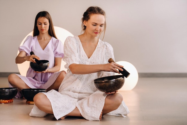 Twee vrouwelijke yogadocenten spelen een Tibetaanse kom in de sportschool tijdens een yoga-retraite