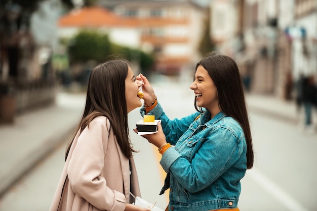 Twee vrouwen die door de moderne stad lopen en verse poffertjes eten. Selectieve focus. Foto van hoge kwaliteit