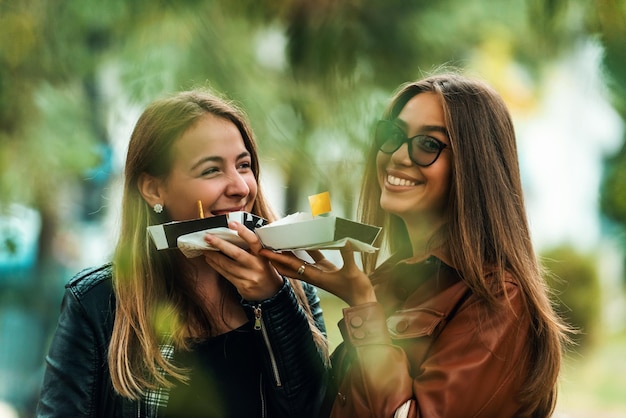 Twee vrouwen die door de moderne stad lopen en verse poffertjes eten Selectieve focus