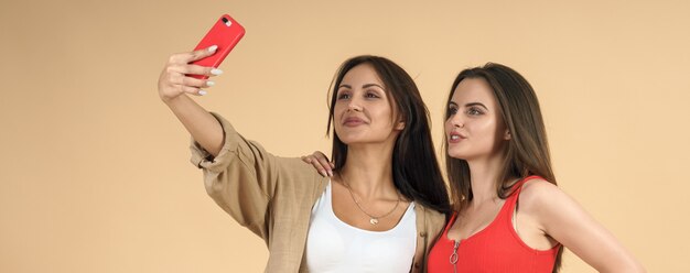 Twee vrouwen die mobiele selfie op beige muur nemen