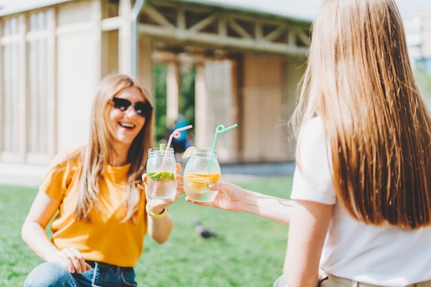 Twee vrouwen die op het gras met limonadecocktails zitten