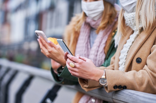 twee vrouwen die smartphones gebruiken en maskers dragen in de stad