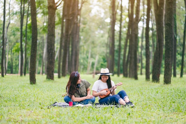 Twee vrouwen die ukelele spelen terwijl ze samen in het bos zitten