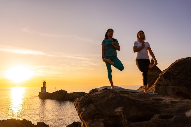 Twee vrouwen doen meditatie en yoga-oefeningen in de natuur aan zee bij zonsondergang gezond en naturistisch leven pilates buitenshuis