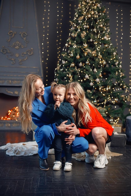 Twee vrouwen en een klein meisje staan bij de kerstboom en knuffelen