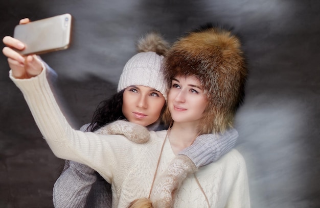 Twee vrouwen in bont wintermutsen kijken naar smartphone.