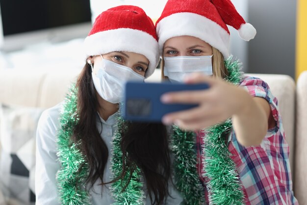 Twee vrouwen in de hoeden van de Kerstman en medische beschermende maskers worden op het portret van de telefooncamera gefotografeerd