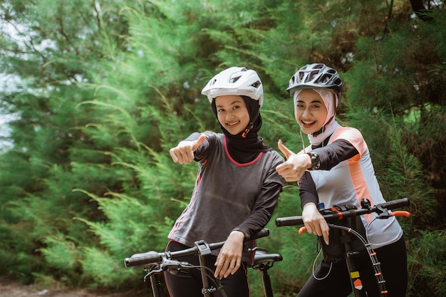 Twee vrouwen in hoofddoek met duimen omhoog terwijl ze samen fietsen