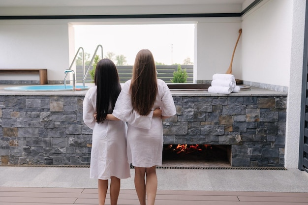 Twee vrouwen in witte gewaden staan voor een bubbelbad met uitzicht op het zwembad en de spa.