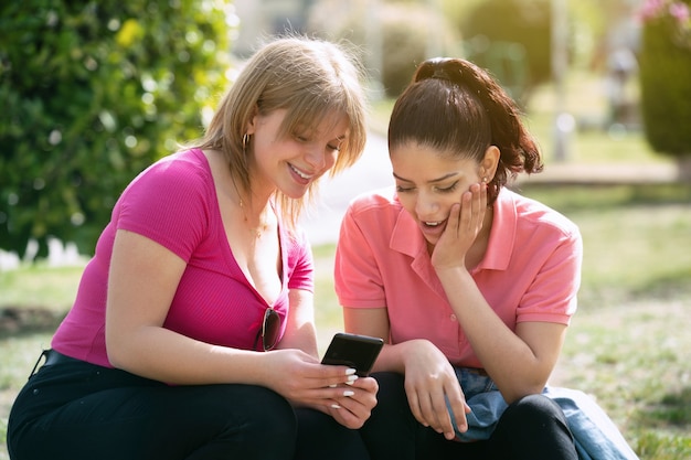 Twee vrouwen Latina in het park kijken naar mobiele telefoon op een zonnige dag