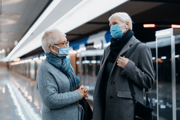 Twee vrouwen met beschermende maskers staan te praten op het metroperron