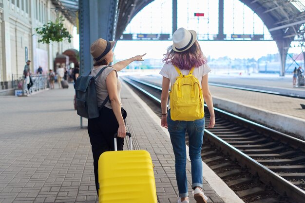 Twee vrouwen moeder en tienerdochter wandelen met bagage op treinstation. mensen wachten op de komst van treinen, achteraanzicht