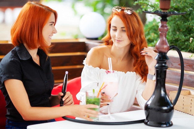 Twee vrouwen roken een waterpijp en genieten van cocktails in een café op straat