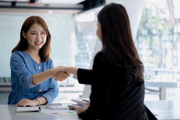 Twee vrouwen schudden elkaar de hand Twee zakenvrouwen schudden elkaar de hand terwijl ze elkaar ontmoeten om brainstorm- en marketingplannen te bespreken om winstgevendere manieren te vinden om te groeien Ideeën voor bedrijfsbeheer voor winstgevende groei