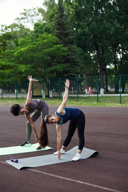 Twee vrouwen van verschillende nationaliteiten warmen zich op voordat ze buiten gaan trainen Spieren opwarmen voor krachttraining of joggen