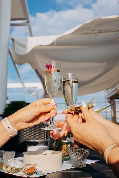 Twee vrouwenvrienden die verse oesters eten en gekoelde proseccowijn drinken op de zomerzonsondergang in restaurant zeevruchtendelicatessen