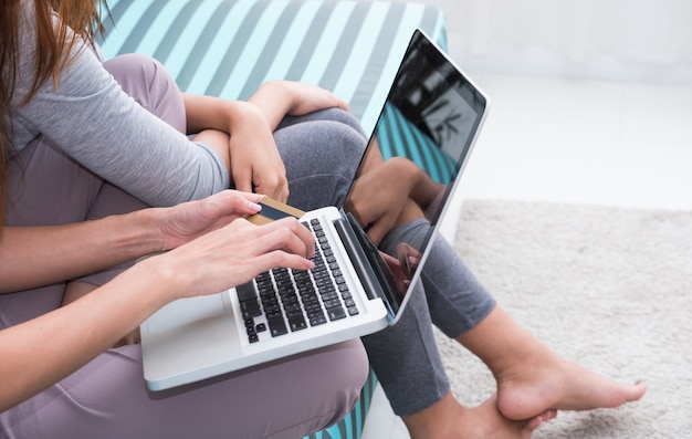 Twee vrouwenvrienden gebruiken creditcard online winkelend met laptop computerzitting op bank