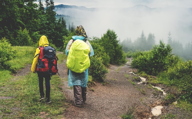 Twee wandelaars toeristen in regenjas lopen op pad naar groen bergbos in de mist met het geel