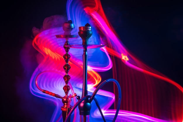 Twee waterpijpkommen met shisha-houtskool met rokerige rook met blauw-rode neonlichten op een zwarte achtergrond