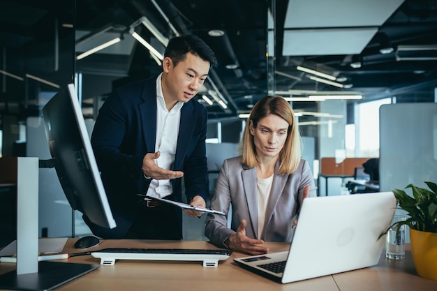 Twee werknemers in een modern kantoor, een Aziatische man en een vrouw die aan tafel werken, collega's bespreken en overleggen over een gezamenlijk project