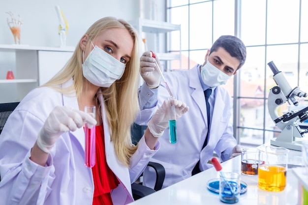 Twee wetenschappers dragen een hygiënisch beschermend masker en werken terwijl ze naar de reageerbuis kijken met een monster in een chemisch laboratorium. Wetenschappers doen onderzoek op de achtergrond van de laboratoriumanalyse