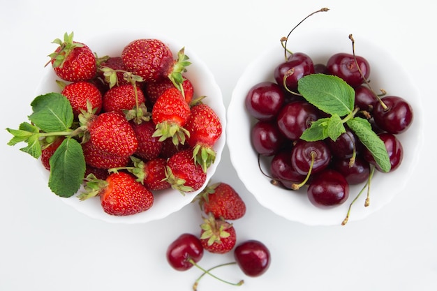 Twee witte borden met kersen en aardbeien met muntblaadjes staan op een witte achtergrond