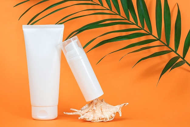 Twee witte lege cosmetica flessen, zeeschelp en groene palmbladeren op oranje oppervlak