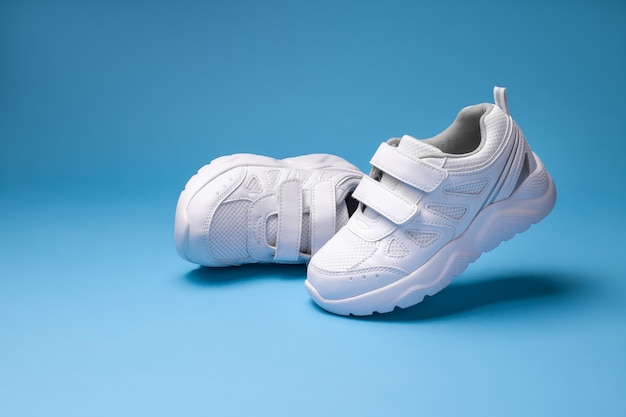 Twee witte meisjessneakers één sneaker die in de lucht vliegt en de andere die op zijn kant ligt geïsoleerd op een...