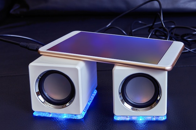 Foto twee witte mini-speakers, van kubusvorm, met blauwe led-lampjes, zijn aangesloten op een smartphonekabel.