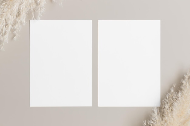 Foto twee witte uitnodigingskaarten mockup met een pampasdecoratie op een beige tafel 5x7 verhouding vergelijkbaar met a6 a5