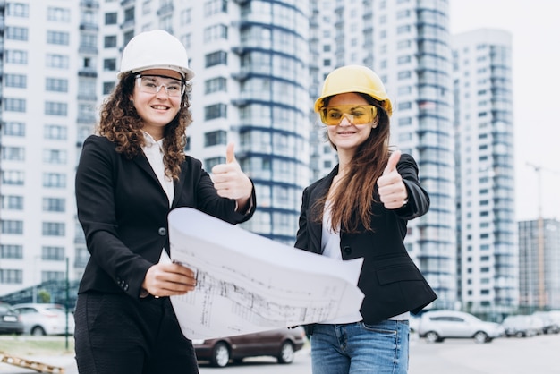 Twee zakelijke vrouwen in beschermende helmen en veiligheidsbril kijken naar bouwschema&#39;s, architectonisch concept